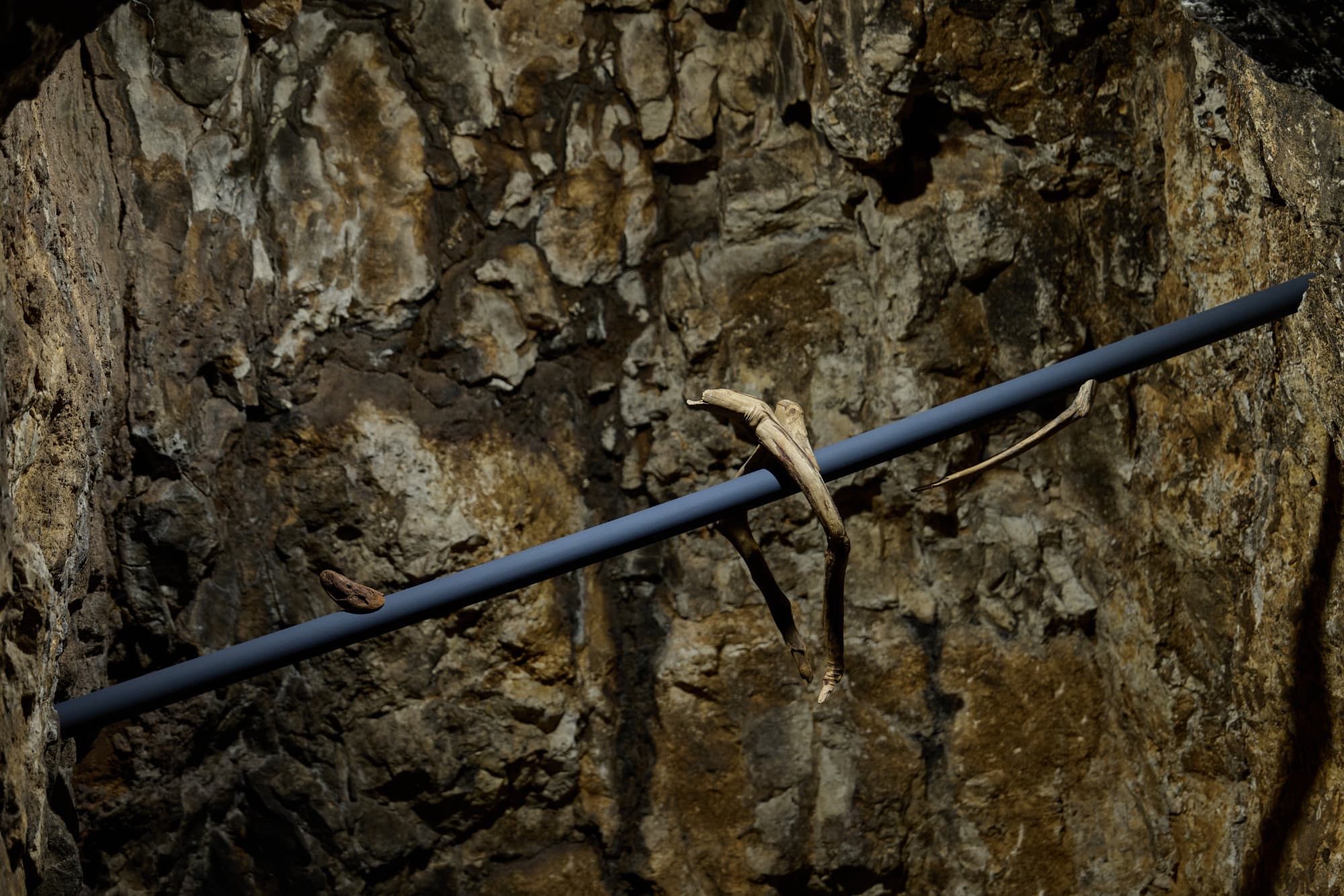 Dettaglio di Props: forme di legno di recupero come ossa lungo l'asta blu, contro la roccia.