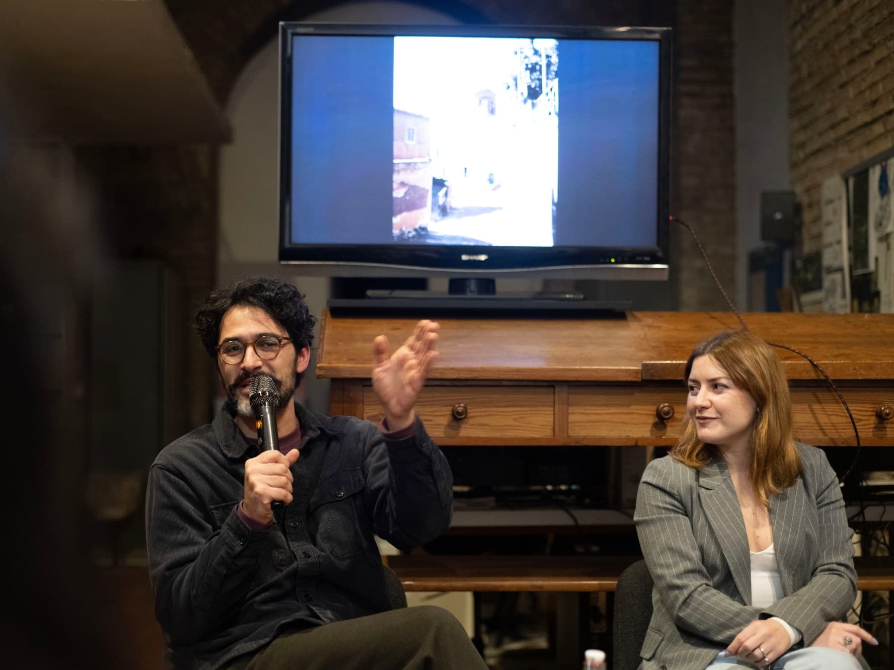 Conversazione pubblica durante ALCOVE: un relatore al microfono accanto alla curatrice.