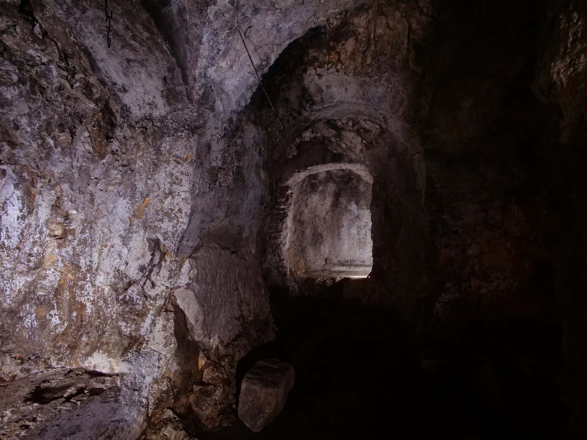La grotta naturale di Studio Specus, con le pareti rocciose illuminate e il passaggio verso una nicchia.